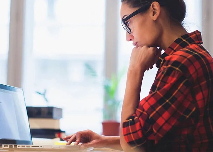 woman with glasses looking at laptop
