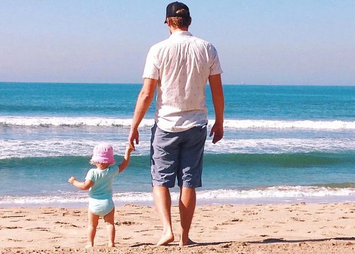 man holding little child hand at beach